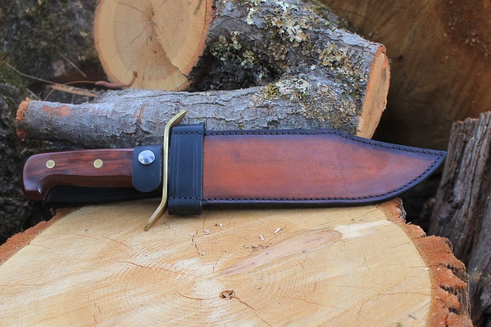 A fixed-blade knife resting on a log beside its hand-stitched leather sheath