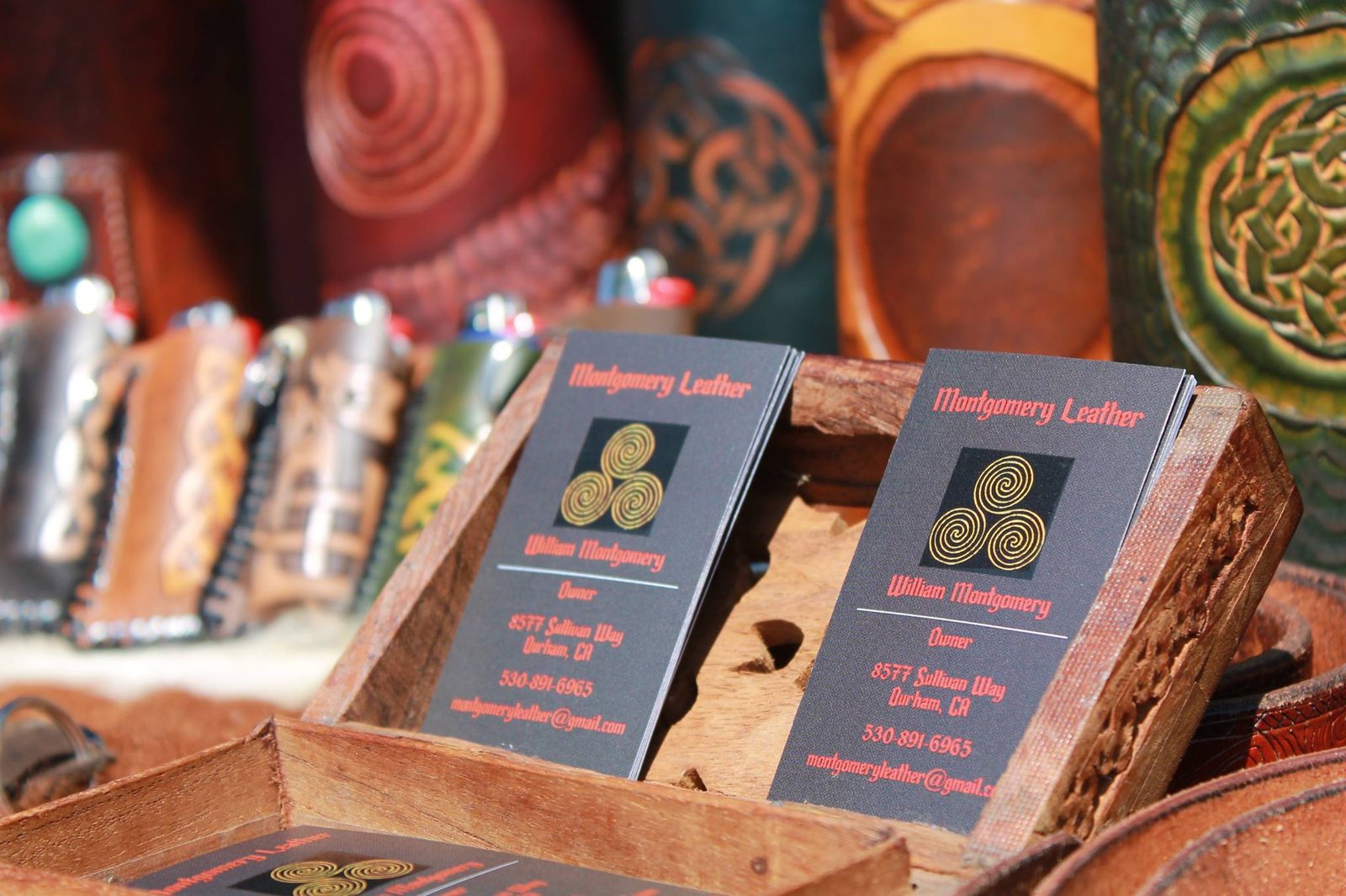 A market table laid with tooled leather cuffs, coasters and a wooden holder of Montgomery Leather business cards
