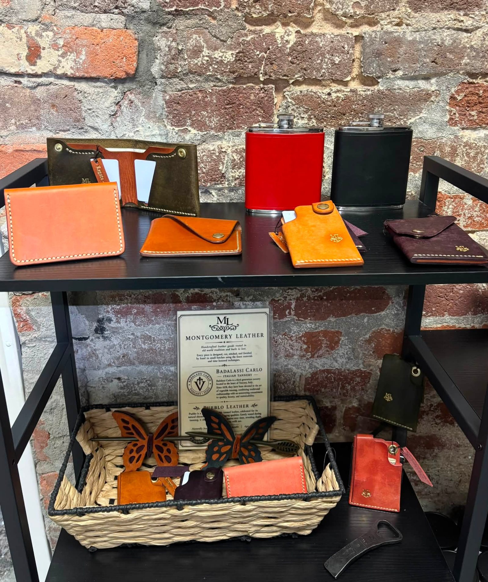 A display table of finished wallets and card cases in orange, red, black and tan against a brick wall