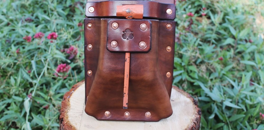 The Paul Bunyan Wedge Pouch standing upright on a cut log, its riveted flap closed over a copper-toned pull