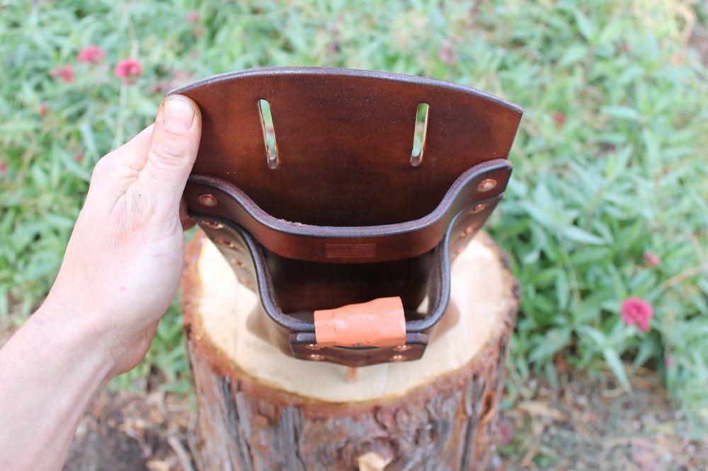A hand steadying the open wedge pouch, showing the stitched interior and the two belt slots cut through the back