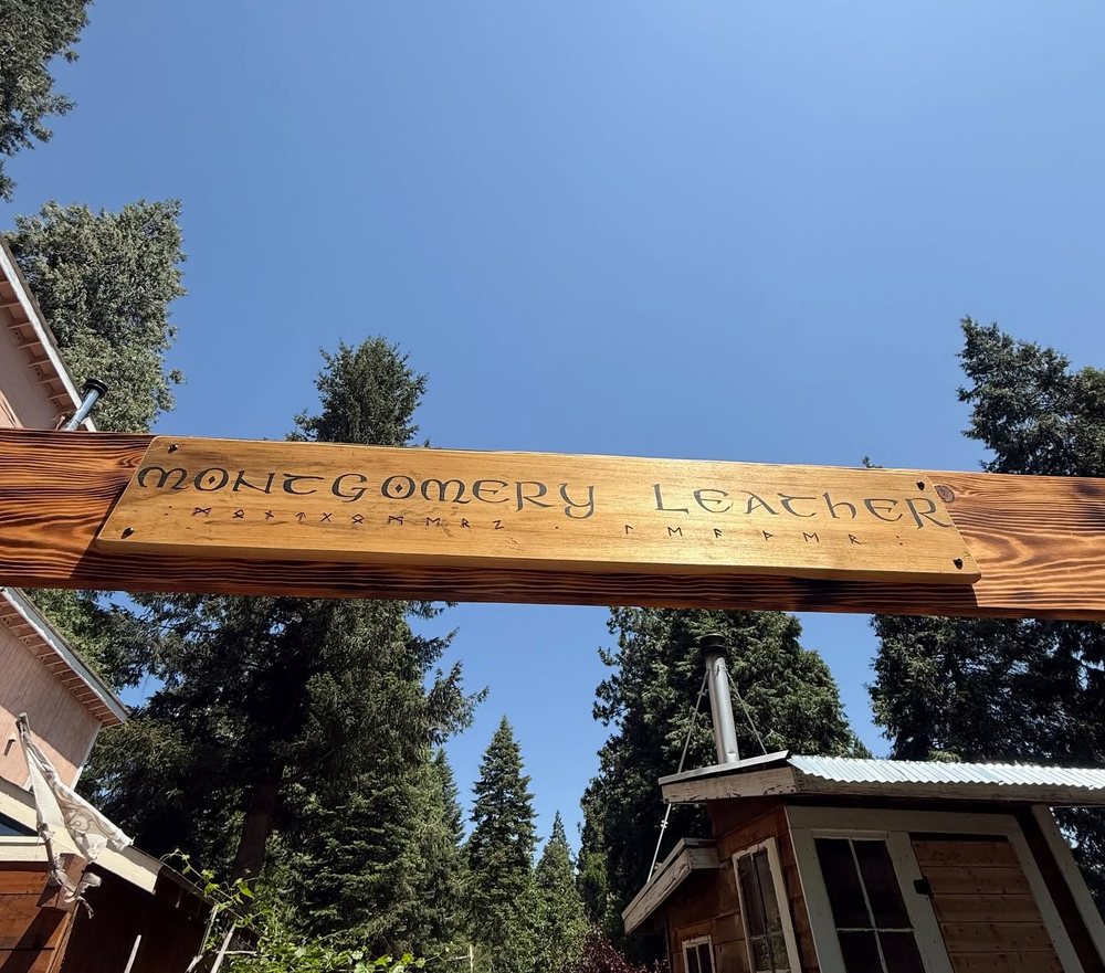 The carved wooden Montgomery Leather sign mounted on a beam against a clear sky